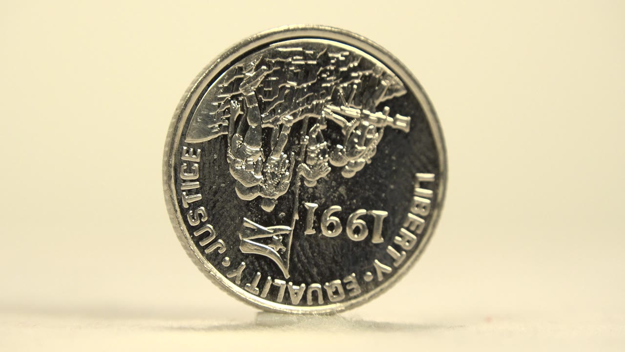 The coin remains upright and centered, with reflective highlights across the engraved text side and no visible people.