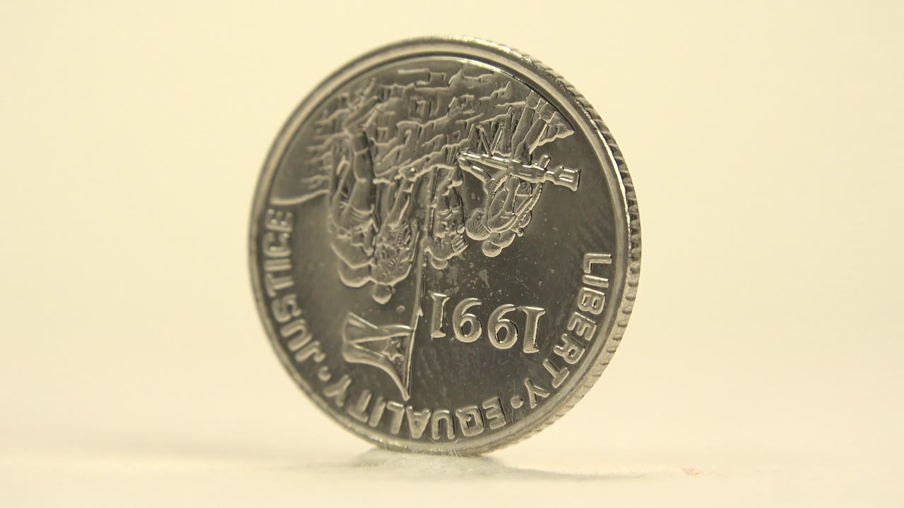 Upright silver coin beginning to turn away from the camera.