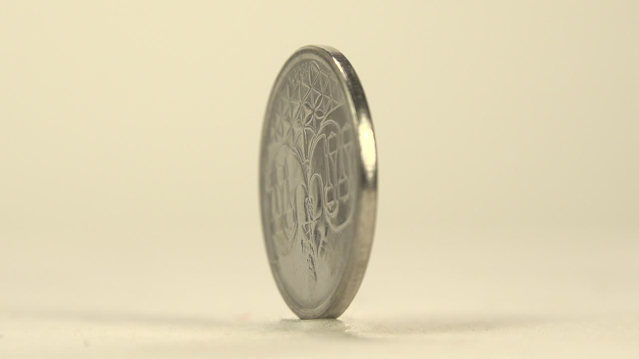 A Brazilian coin stands nearly edge-on on a pale tabletop with its reverse design faintly visible against a warm cream background, no visible people.