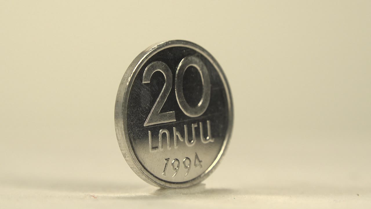 The coin has rotated to reveal a front face with a large 20, embossed script, and the date 1994 under warm soft light, with no visible people.
