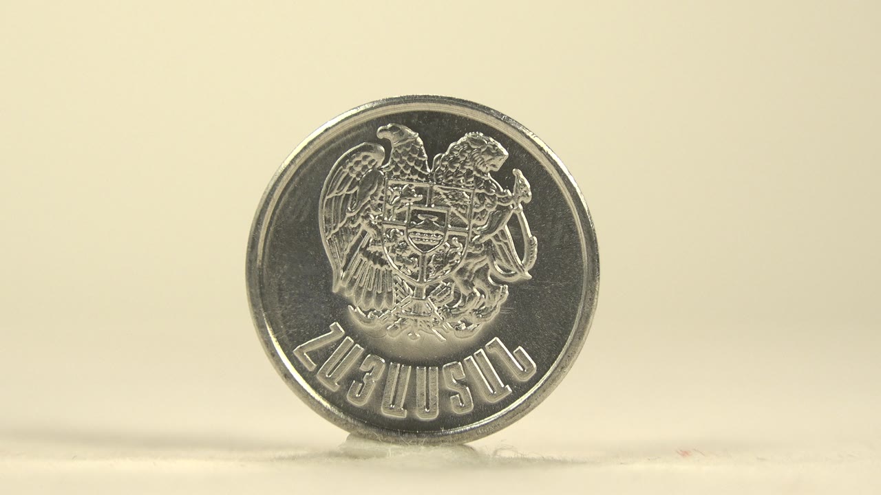 A silver coin stands upright on a cream tabletop with an embossed emblem facing the camera and no visible people.