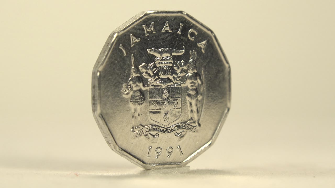 The coin faces the camera with JAMAICA, a coat of arms, and the 1991 date readable on the metal surface, set against a plain cream background with no visible people.