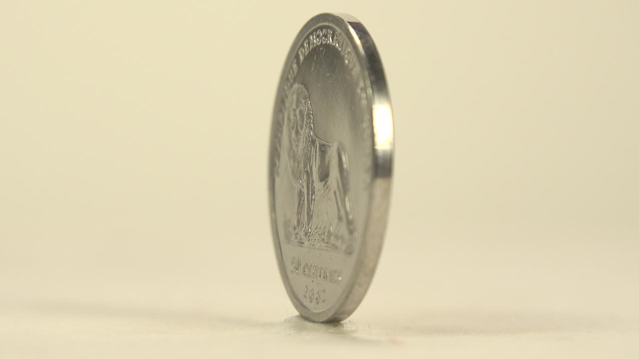 Silver coin standing on edge on a pale surface.