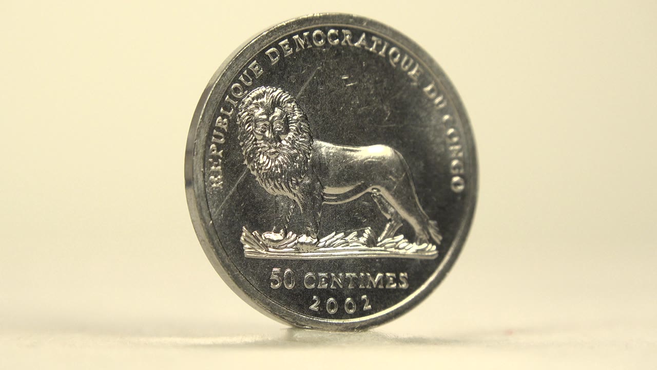 An upright reflective 50 centimes coin shows a lion design and 2002 date on a pale tabletop, with a soft cream background and no visible people.