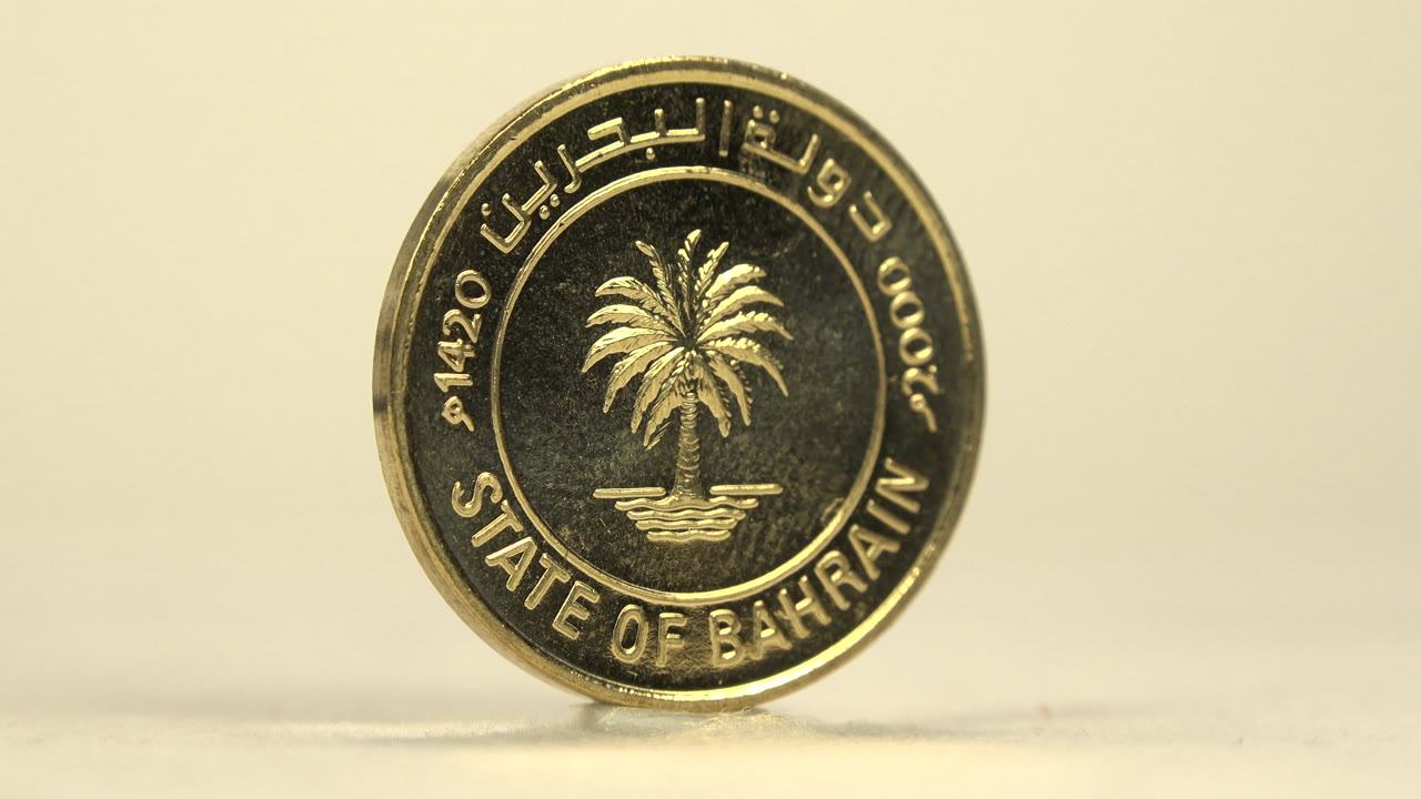 The coin faces the camera more directly, showing the palm tree emblem, Arabic script, the year 2000, and the English words State of Bahrain, with no visible people.