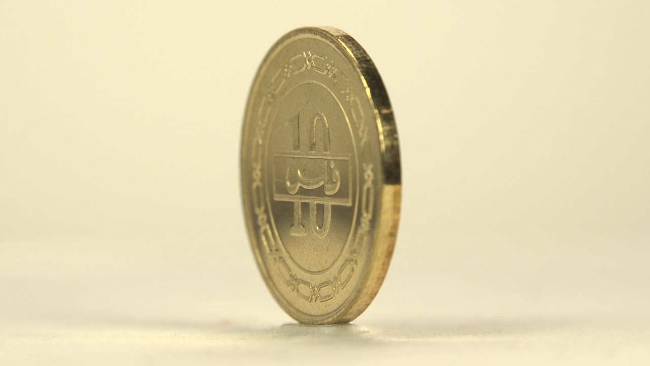 The coin has rotated to a narrow side angle, with its ridged golden edge catching light and the front design partly visible, with no visible people.