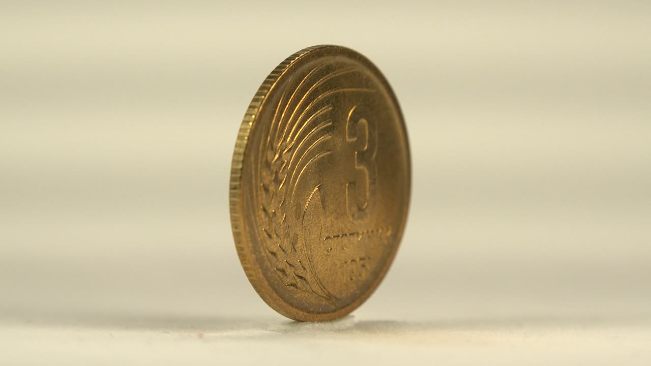 The coin has turned enough to show a bronze face with the number 3, raised markings, and Cyrillic lettering on a pale reflective surface with no visible people.