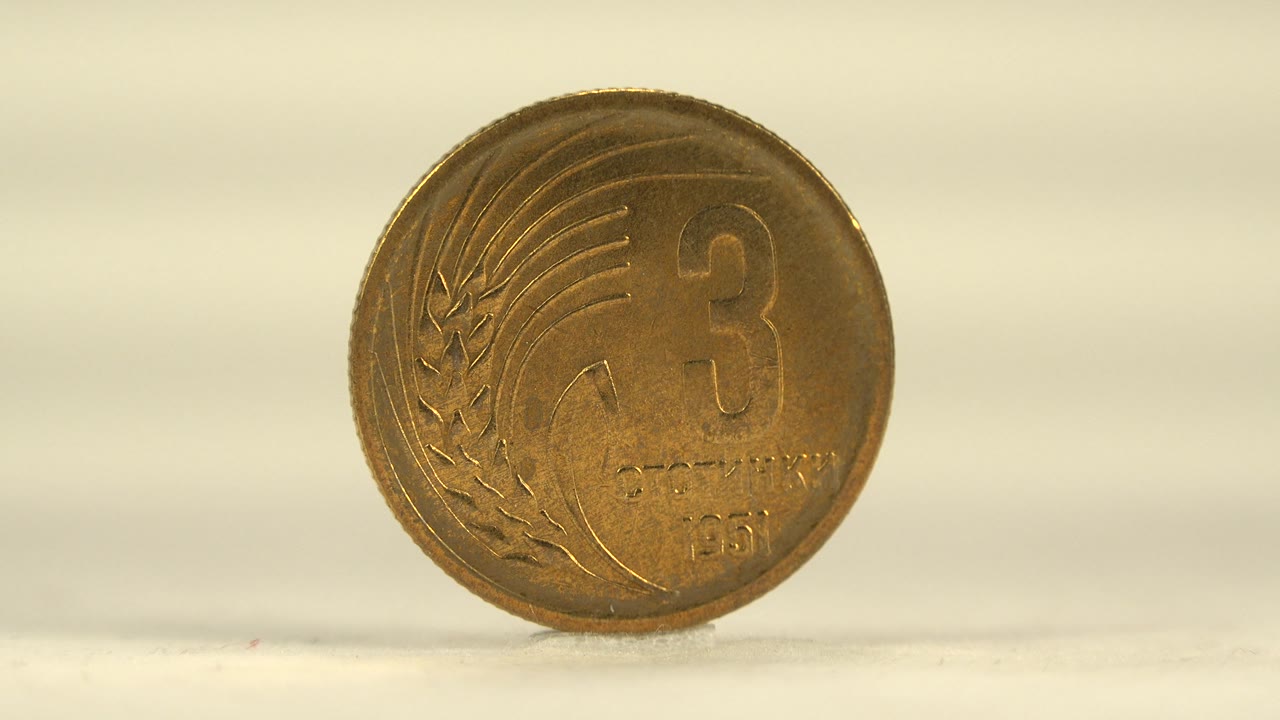 A larger face view of the coin shows the number 3, decorative grain detail, warm bronze color, and a soft shadow on the pale surface with no visible people.