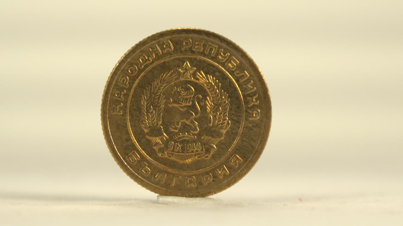 A gold-colored coin stands upright on a pale surface with its crest side facing the camera and no visible people.