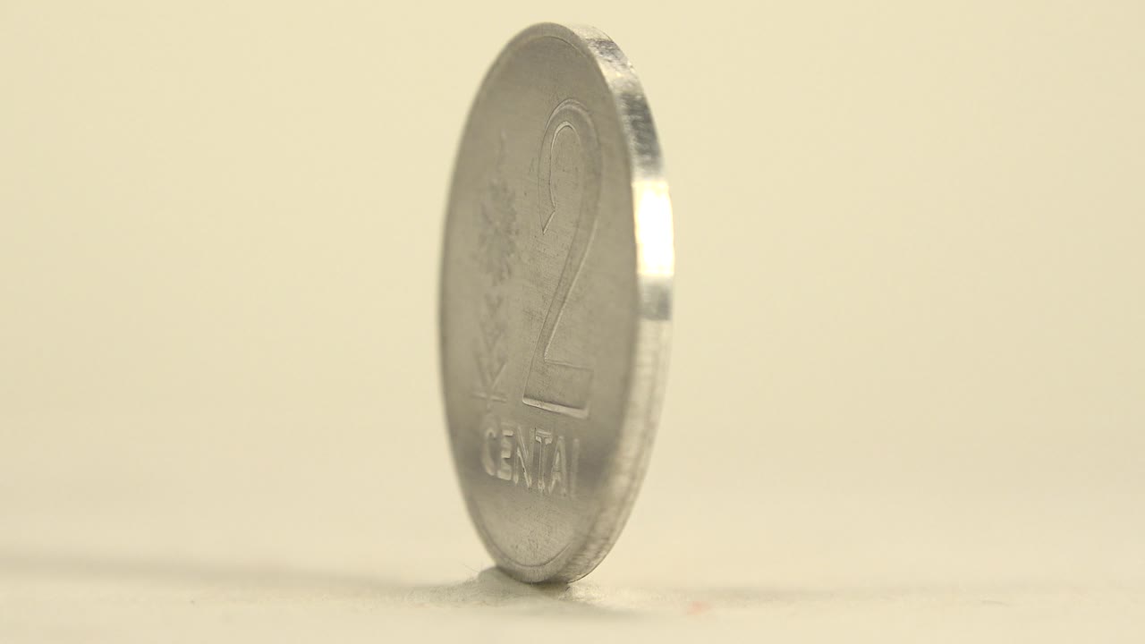The coin remains upright on its rim, with the large number 2 and centai lettering visible through soft focus and no visible people.