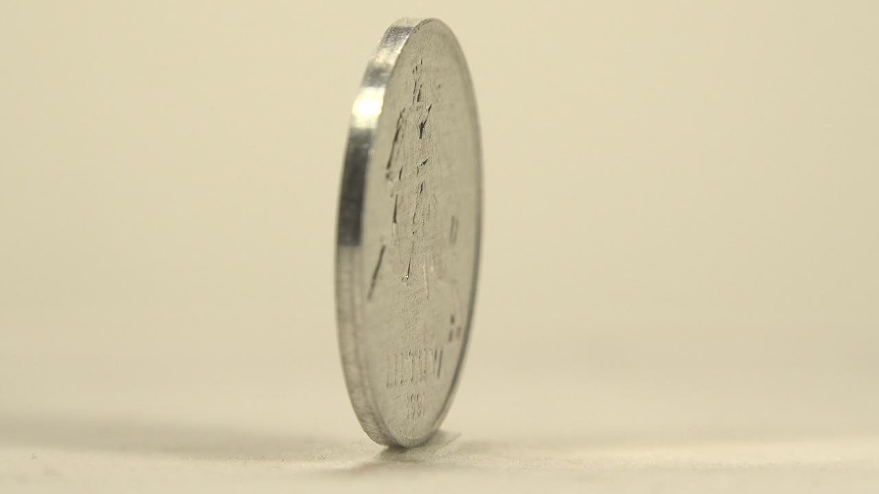 The silver coin is seen mostly from the edge, with a narrow profile, bright rim highlight, and no visible people.