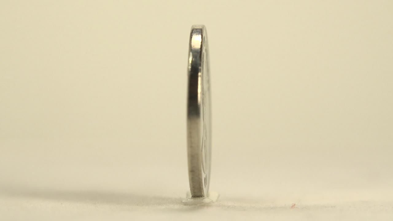 Silver coin still mostly edge-on against a plain cream background.