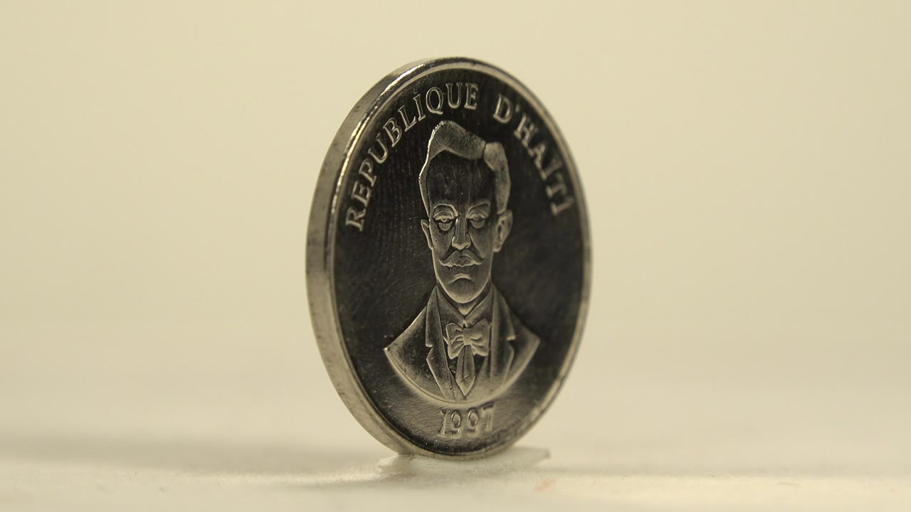 The coin turns toward the camera, showing a portrait side with the text Republique d'Haiti and the date 1997, with no visible people.