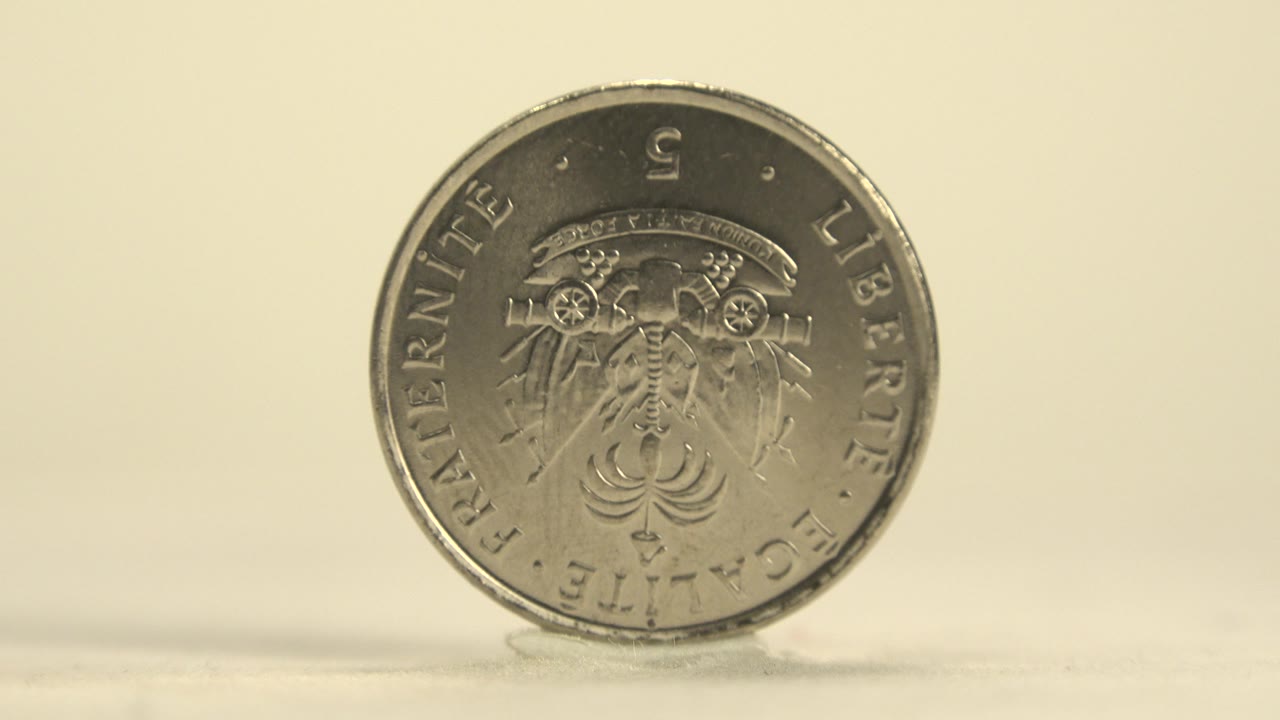 Silver Haitian coin in Haiti remains upright with the emblem side forward, catching slightly different highlights on the rim and raised details, with no visible people.