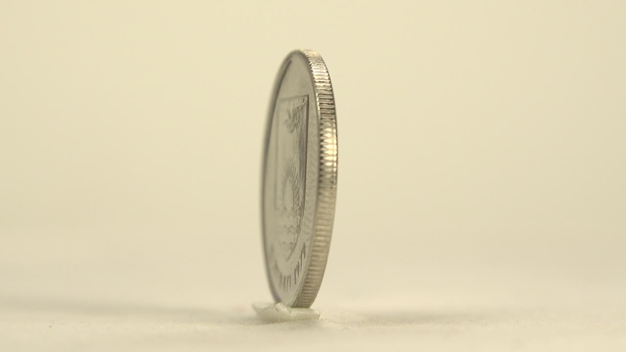 A Kiribati 5 cent coin is seen mostly edge-on while standing on a pale flat surface, with soft warm light and no visible people.