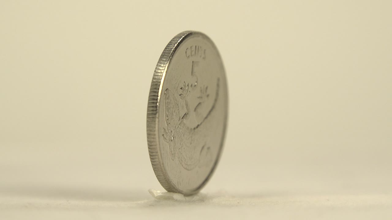 The spinning coin tilts toward camera so part of the Kiribati face and rim are visible, resting on a pale surface with no visible people.