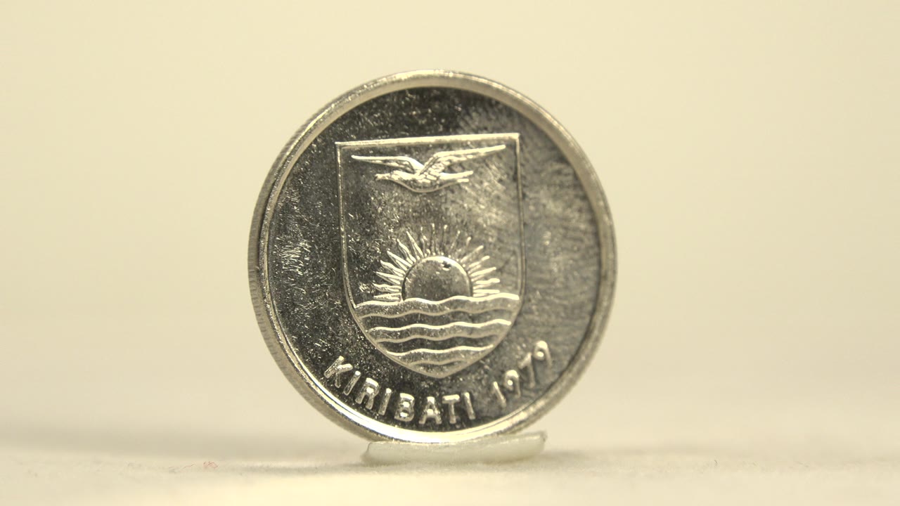 Front-facing silver coin on a clear support shows the Kiribati crest side with bright reflections across the metal and no visible people.