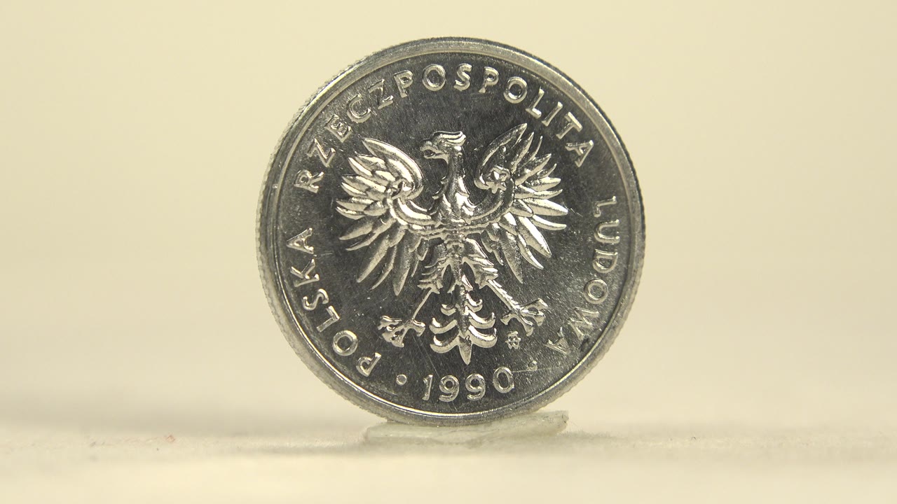 A silver Polish coin stands upright with the eagle side facing camera on a pale reflective tabletop, no visible people.