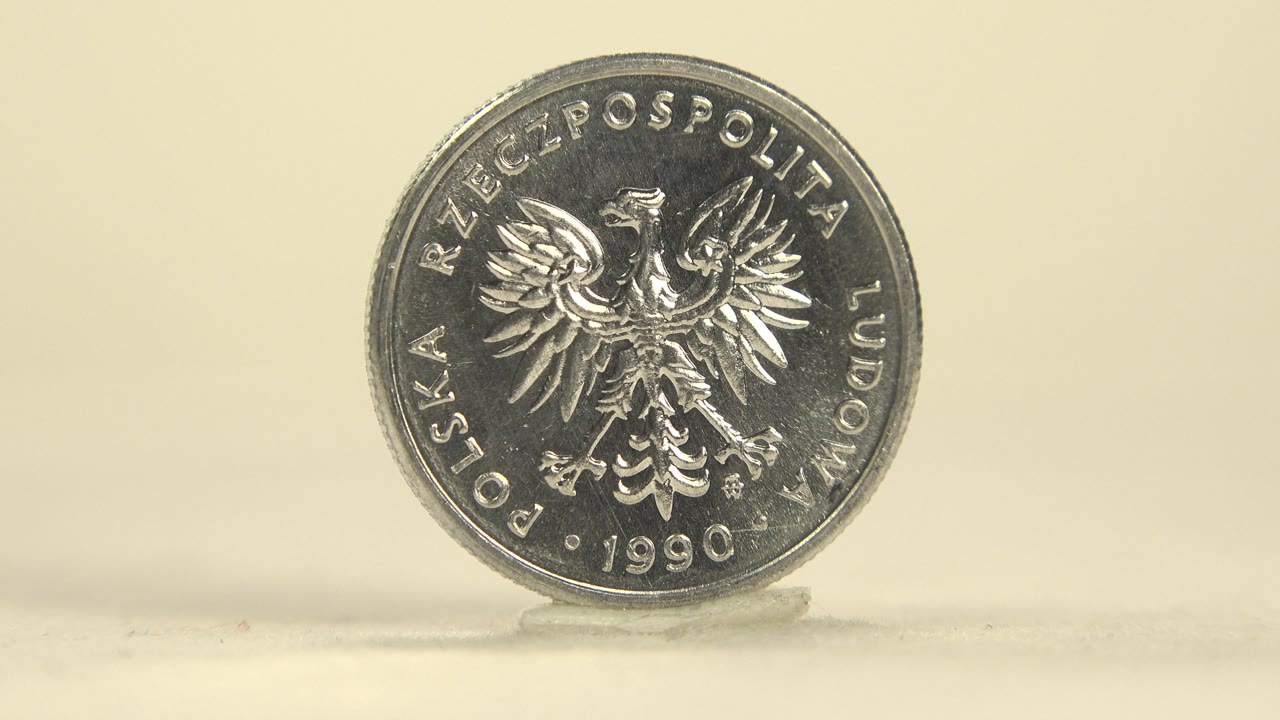 The coin remains upright with the eagle side still visible, catching brighter highlights along its upper rim, no visible people.