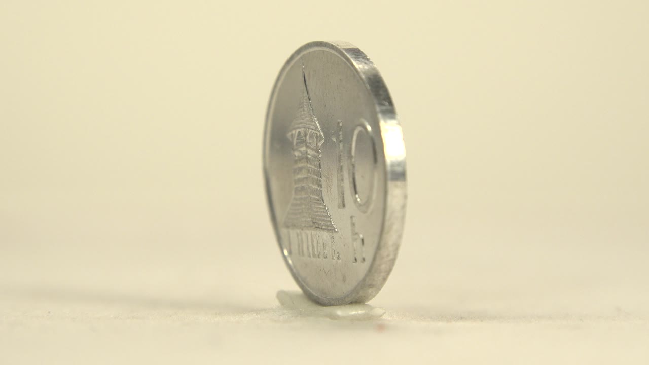 A silver coin stands upright on a cream surface, angled to show part of its face and reflective rim, with no visible people.