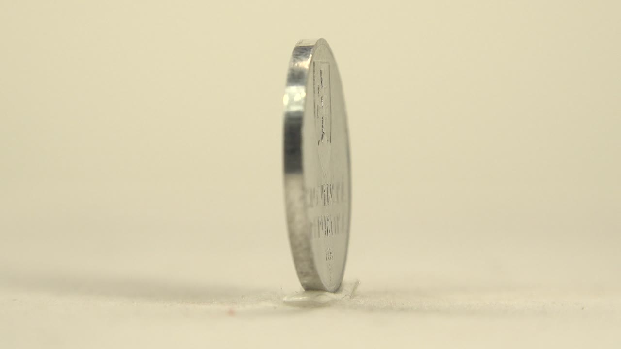 The coin is turned nearly edge-on, showing a narrow reflective profile on the cream surface, with no visible people.
