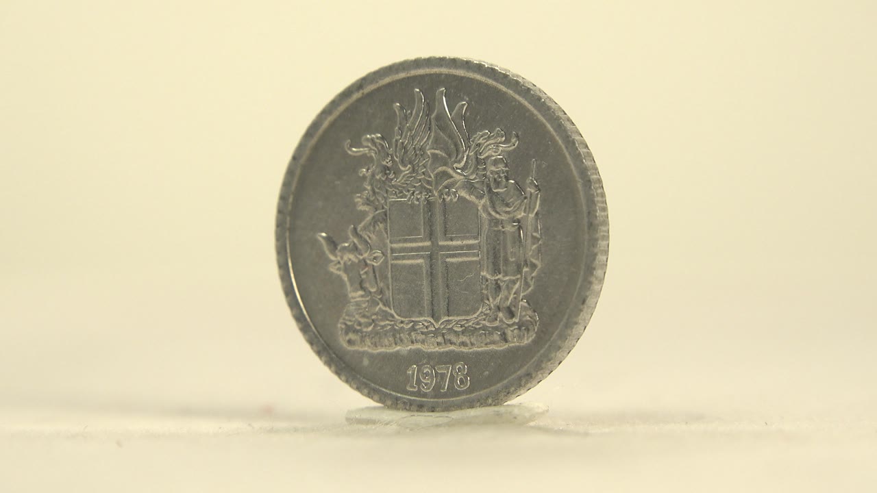 A slightly darker face-on view shows the upright coin with the crest and 1978 still readable, set against the same plain cream background with no visible people.