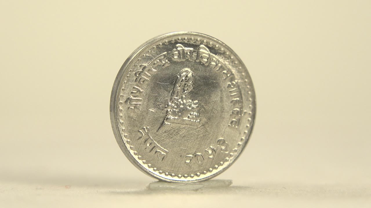 A silver-colored coin stands upright on a pale tabletop in Indiana United States footage, showing one face with raised lettering and no visible people.