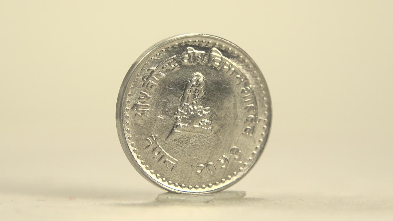 The coin remains upright on the pale surface in Indiana United States footage, with the same face nearly centered and soft highlights across the metal, no visible people.