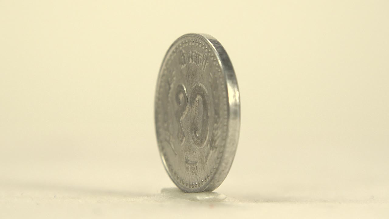 A silver coin stands upright at a slight angle on a pale tabletop with a warm cream background and no visible people.