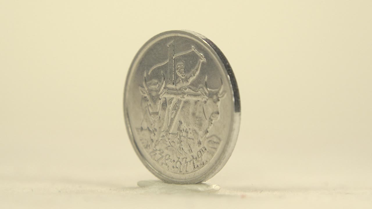 The coin has turned to a shallow angle, keeping the front relief partly visible while the raised rim and narrow side catch brighter light, with no visible people.