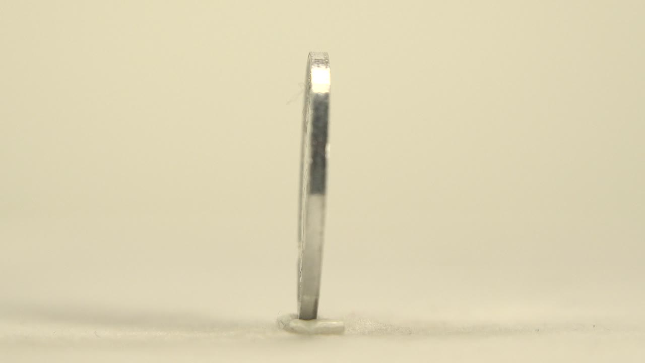 Thin upright coin edge on a pale surface.