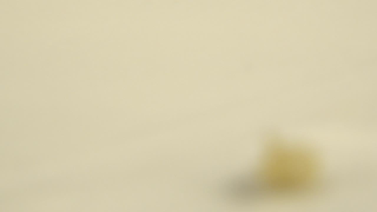 Opening frame shows a light cream flat surface with a heavily blurred yellow shape near the center distance and no visible people.
