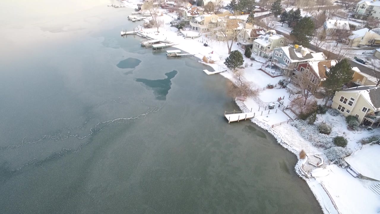 Aerial view of frozen lake edge with snow-covered homes and docks
