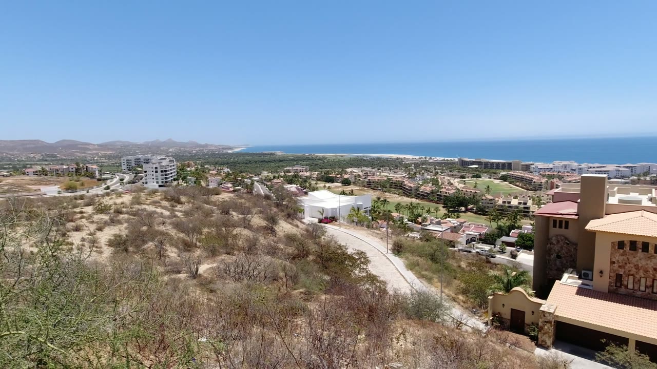 Elevated coastal town view with scrubby foreground and ocean beyond the buildings.