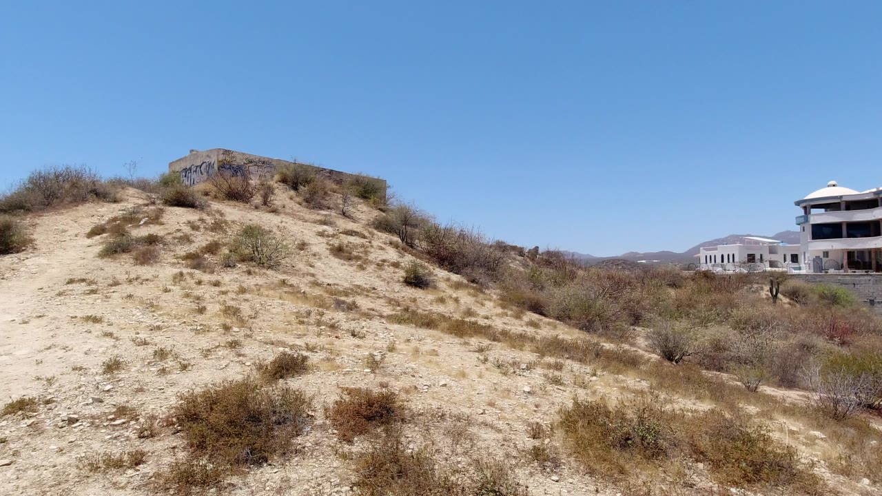 Sandy scrub hill with white buildings at right under blue sky