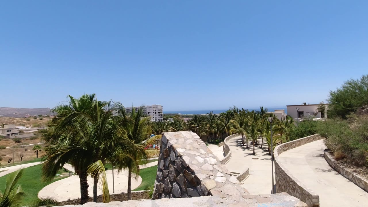 Elevated view of palms, stone walls, paths, hills, and ocean horizon.
