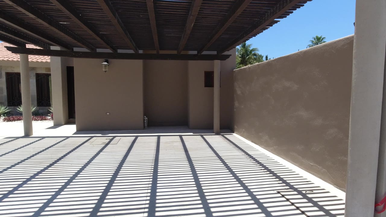 San Jose del Cabo courtyard with strong pergola shadow lines across pale concrete, stucco walls, a roof edge, and no visible people.