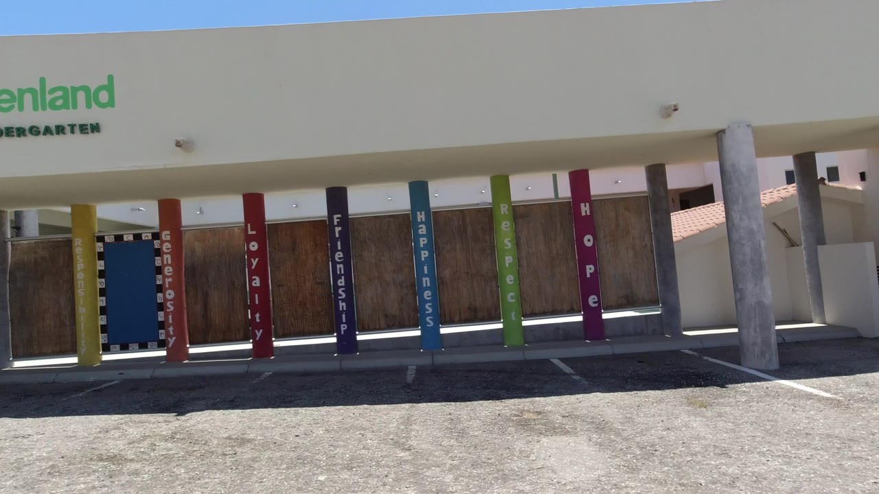 The San Jose del Cabo exterior holds on the kindergarten entrance, showing green signage above multicolored columns and a shadowed gate area with no visible people.