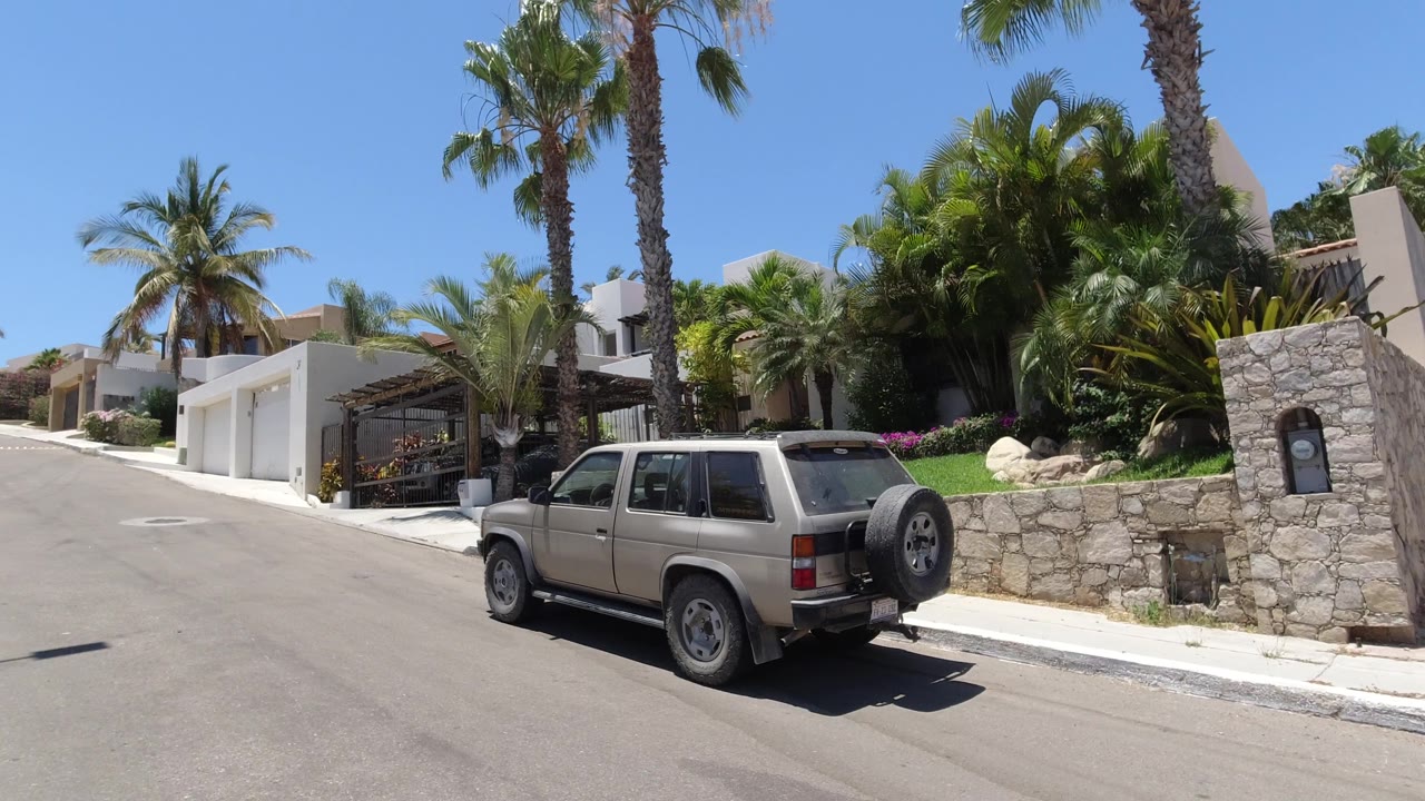 Residential street with parked SUV, palms, and white garage fronts.