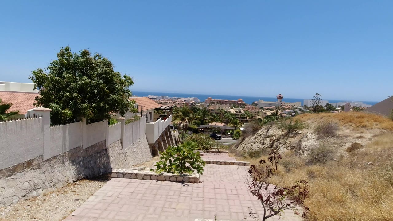 Hillside walkway with white walls, homes, dry grass, and distant ocean