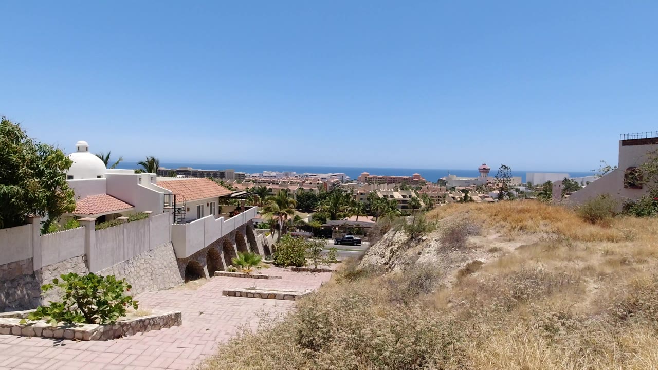 Dry hillside path beside white walls and a distant ocean horizon.