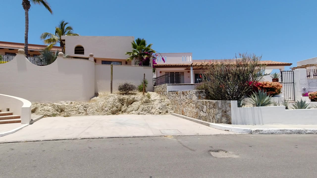 Cream stucco residence behind a low wall on a sunny street
