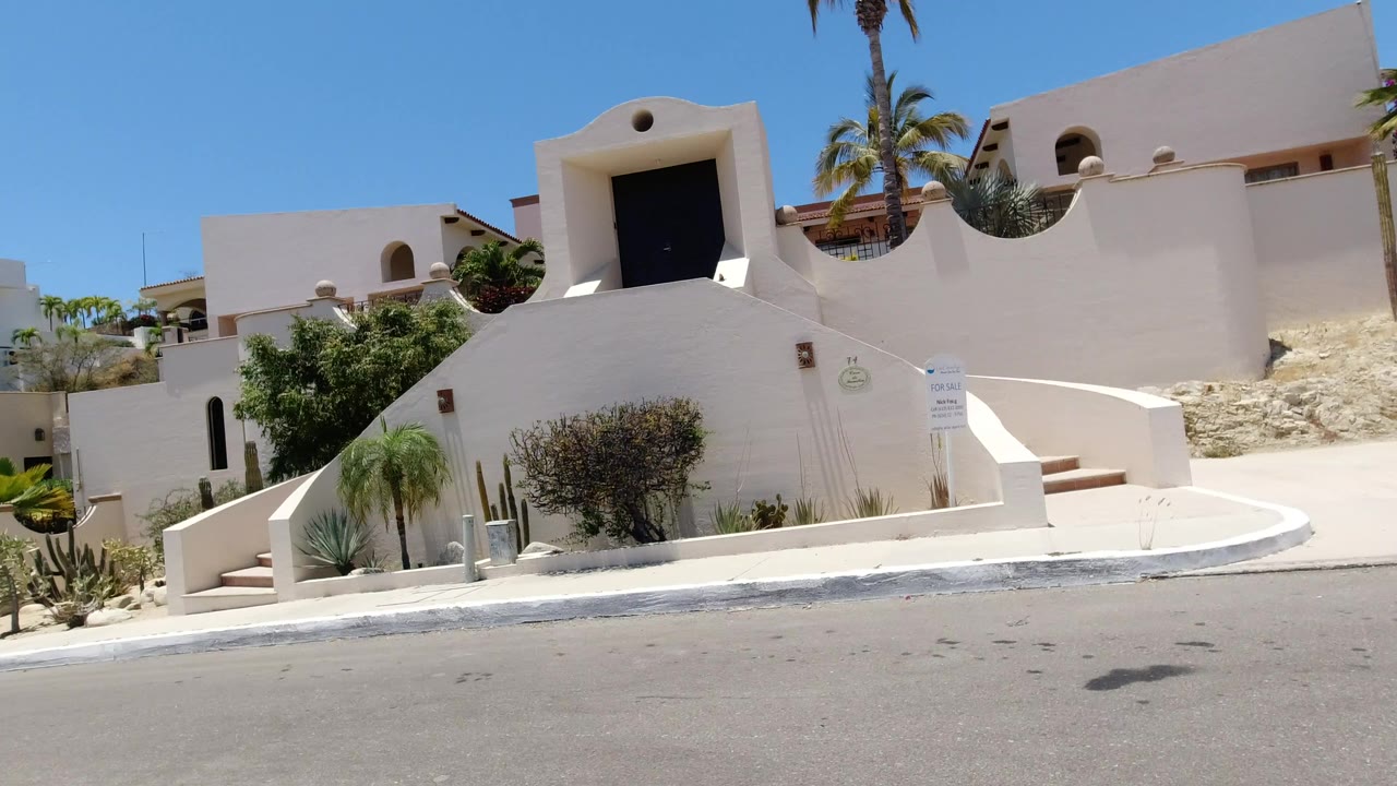 Cream modern building with curved walls, stairs, palms, and an empty street.