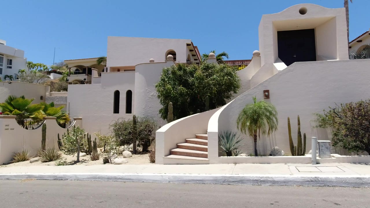 A San Jose del Cabo street view shows white stucco buildings, curved exterior stairs, desert plants, palms, and a clear blue sky with no visible people.
