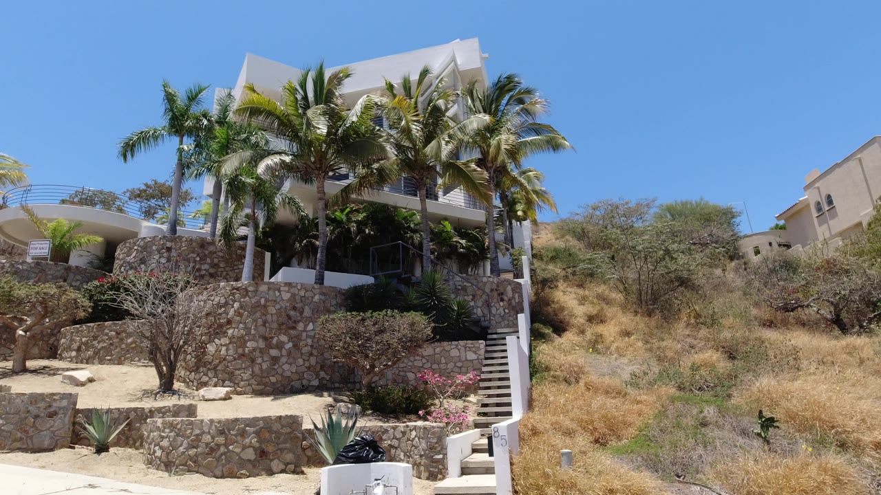 White resort building above stone walls and palm trees under blue sky.
