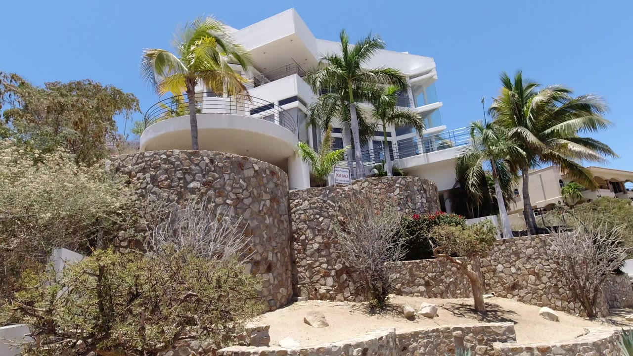 White hillside house above stone walls and palm trees
