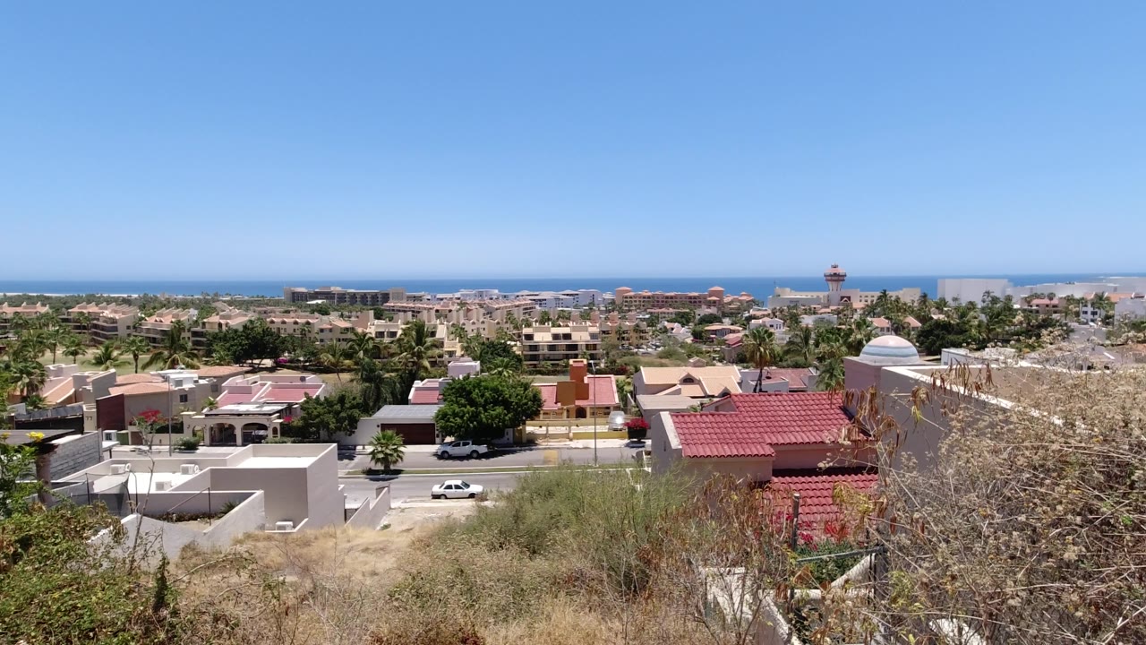 Residential area below a clear sky with dry brush foreground and ocean in the distance.