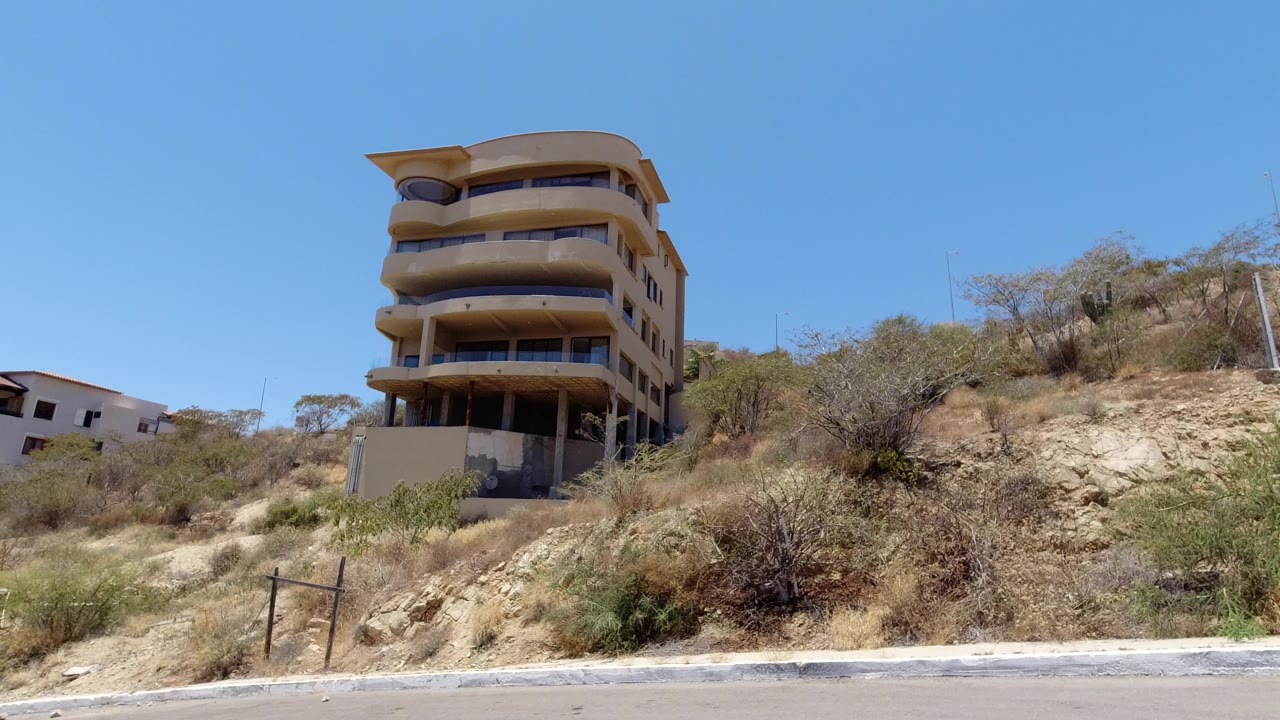 Tall tan building above a dry hillside road