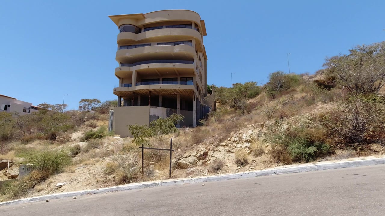 Unfinished apartment building on a dry hillside above a paved road.