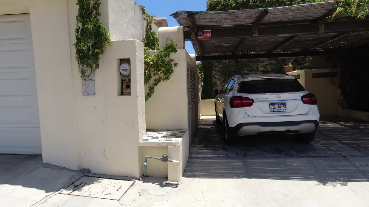 White SUV parked under a shaded carport beside cream stucco garage walls.